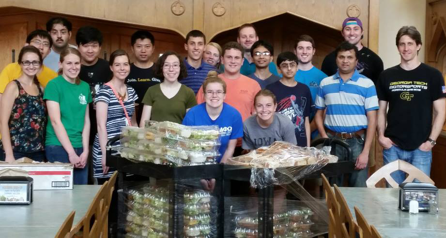 A group of female and male students in front of trays with packed food.