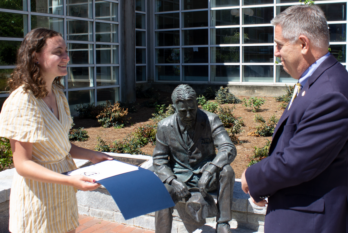 Female student receiving a document from a man with gray hair wearing a suit. 