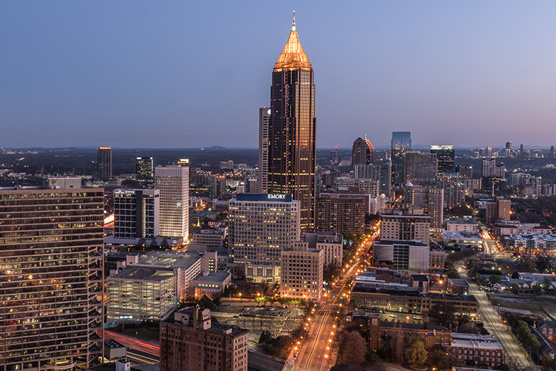 The Atlanta skyline at dusk, with tall buildings silhouetted infront of a pale blue and pink sky