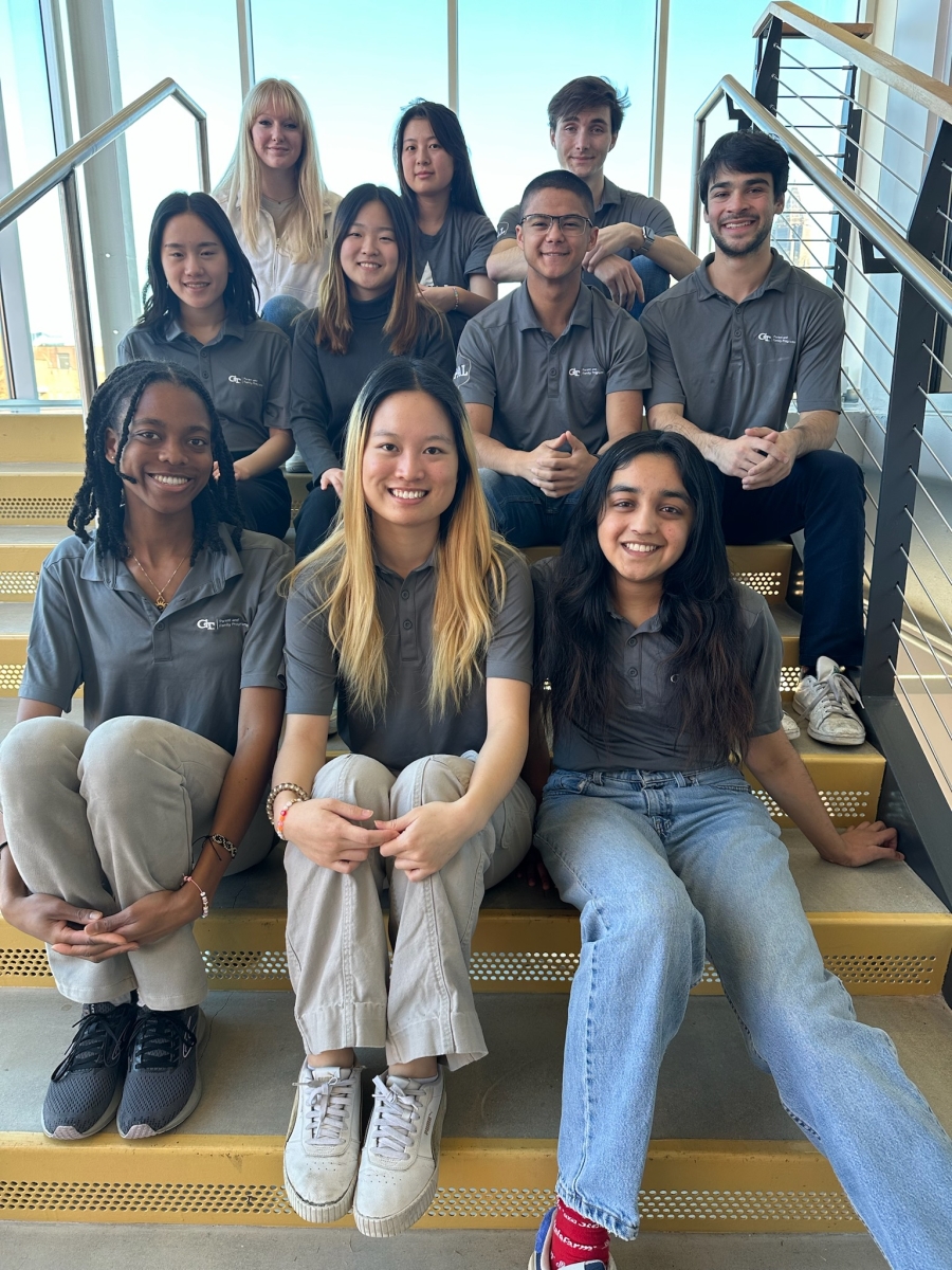 a dozen college students sit on stair steps, three to row, all wearing similar t-shirts